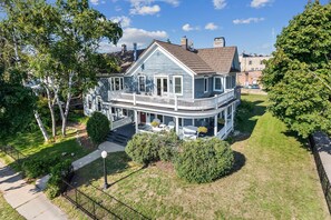 A two-story house with a porch, a lawn, and a fence. - Charming Queen Suite, two person jet tub, downtown (Sturgeon Bay)