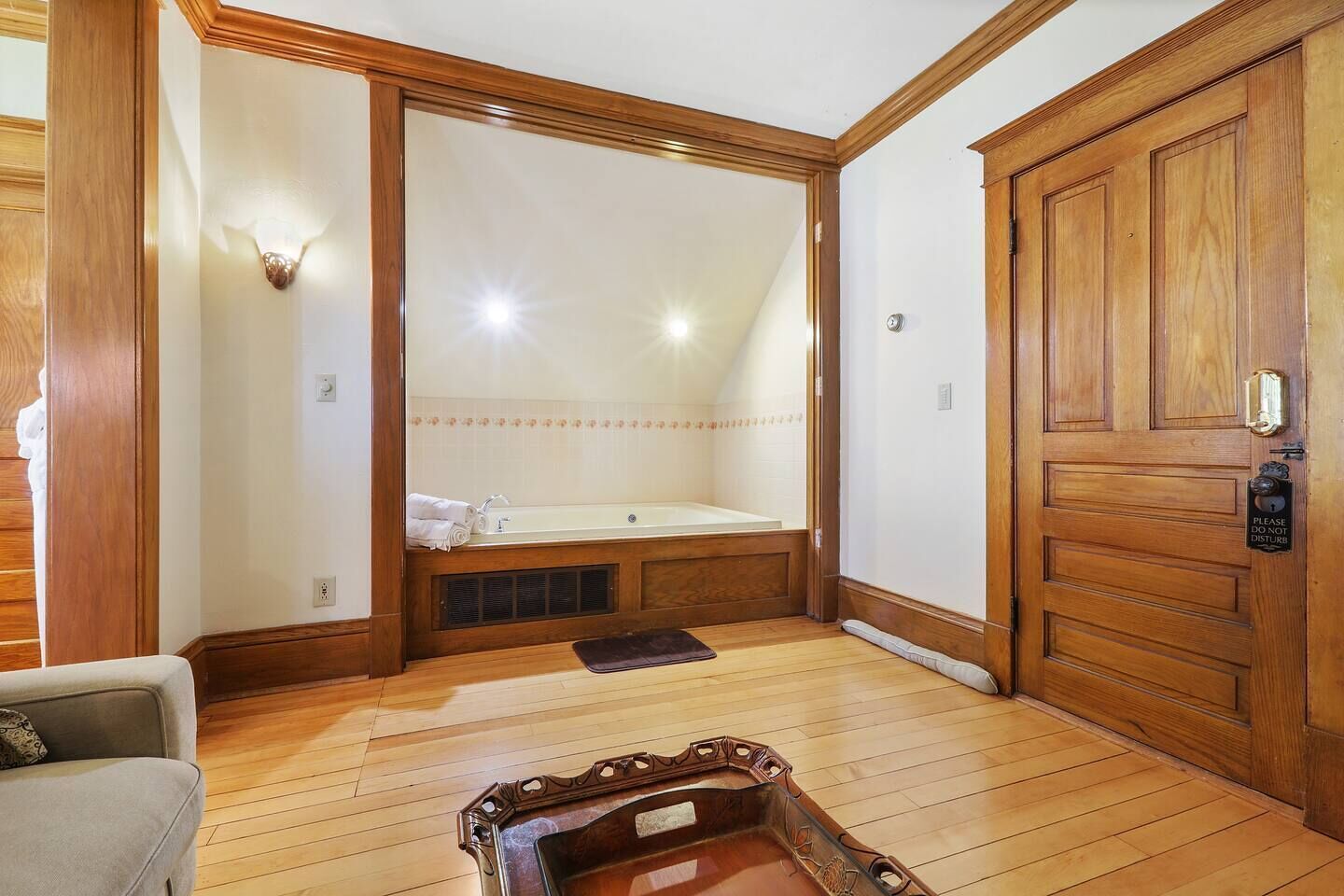 Une pièce avec un plancher en bois, un grand miroir, une porte en bois sur laquelle est apposée une pancarte indiquant « Veuillez ne pas déranger », et une baignoire avec des serviettes.