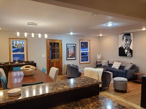 A modern living room with a dining area, featuring a wooden dining table, a sofa set, and a large painting on the wall.