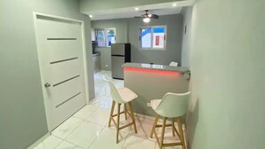 A modern kitchen with a bar area, two white bar stools, and a refrigerator.