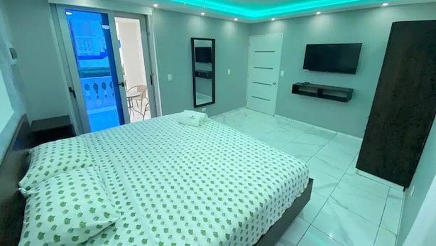A bedroom with a bed, a ceiling fan, a TV, and a door leading to a balcony.