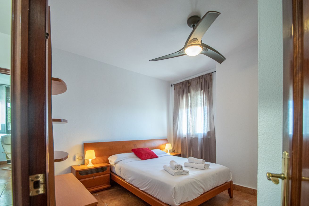 A hotel room with a bed, bedside lamps, a ceiling fan, and a window with curtains.