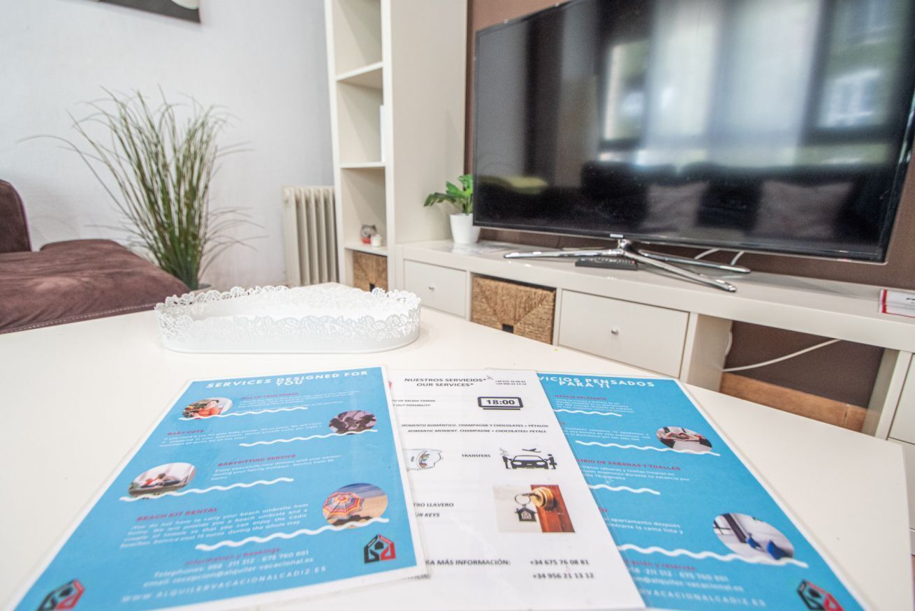 Une pièce avec une table blanche, une brochure, un téléviseur, une plante et un radiateur.