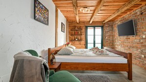 Un dormitorio con cama de madera, un sillón verde, una mesita pequeña y una pared de ladrillo con un televisor.
