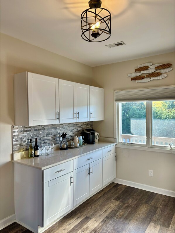 A kitchen with white cabinets, a tiled backsplash, a coffee maker, and a window with a view of greenery. - Gorgeous waterfront 2 bed 2 bath condo full amenities Mariners Landing resort (Huddleston)