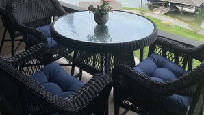 Un patio cubierto con mobiliario de mimbre y vistas a un lago y muelle.