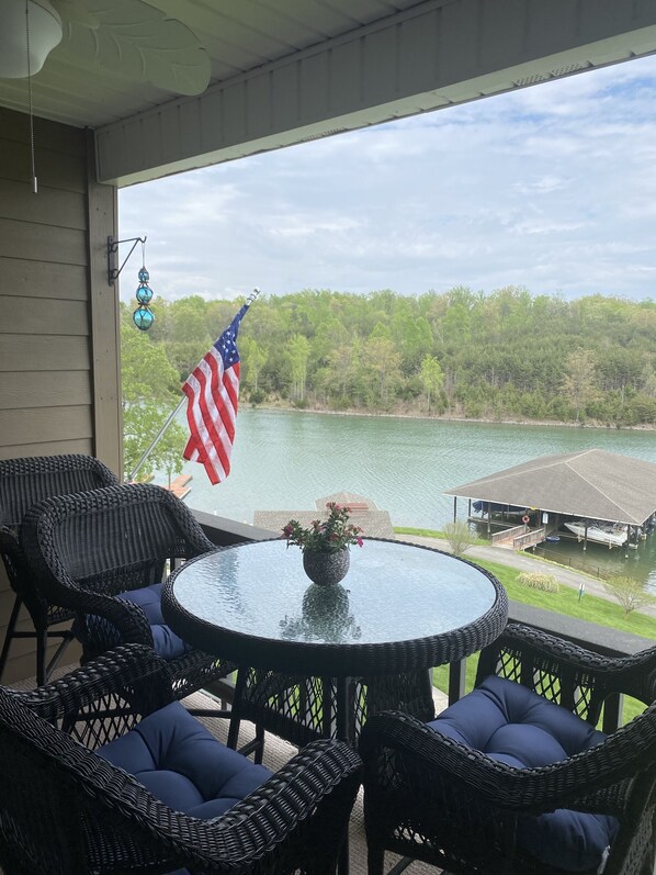 Eine überdachte Terrasse mit Korbmöbeln und Blick auf einen See und eine Bootsanlegestelle.