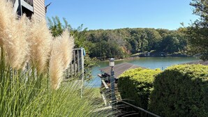 Vista de un lago con un muelle, rodeado de vegetación y un edificio con balcón.