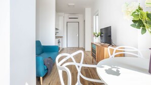 A modern living room with a blue sofa, white chairs, a wooden dining table, and a TV on a wooden cabinet. - Hostmate - Milano - Pirelli - Porta Nuova (Milano)