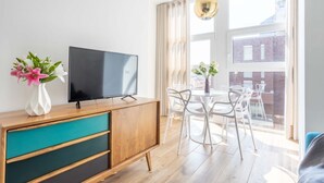 A modern living room with a TV on a wooden cabinet, a dining table with chairs, and a large window with curtains. - Hostmate - Milano - Pirelli - Porta Nuova (Milano)