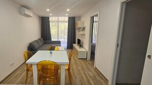 Un espace de vie compact comprenant un coin repas, un canapé, un téléviseur et une petite kitchenette.