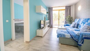 Un salon moderne avec un canapé, un téléviseur et un balcon agrémenté de rideaux.