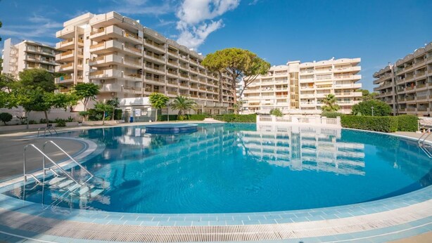 Une grande piscine entourée d’immeubles résidentiels à plusieurs étages dotés de balcons, un ciel dégagé et quelques espaces verts.