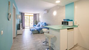 Un espace de vie compact comprenant une kitchenette, un coin repas et une chambre avec une porte coulissante donnant sur un balcon.