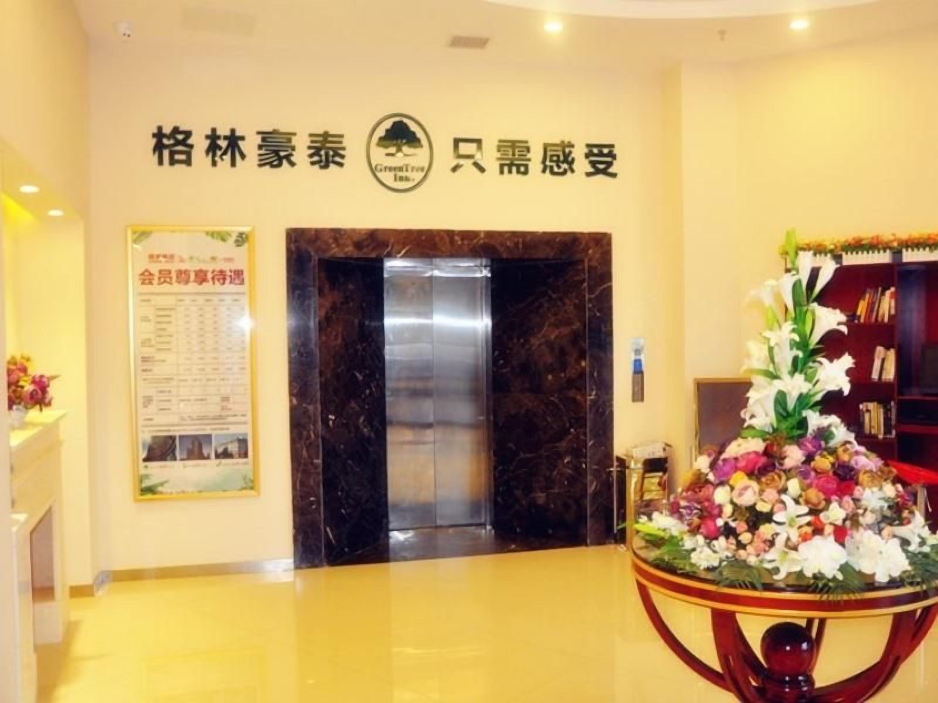 Vestíbulo de hotel con mostrador de recepción, un tablón de anuncios, un ascensor y un arreglo floral.