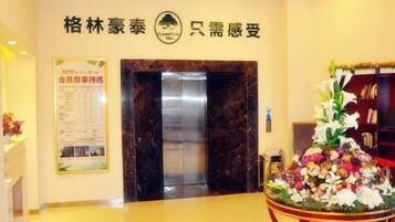 Vestíbulo de hotel con mostrador de recepción, un tablón de anuncios, un ascensor y un arreglo floral.