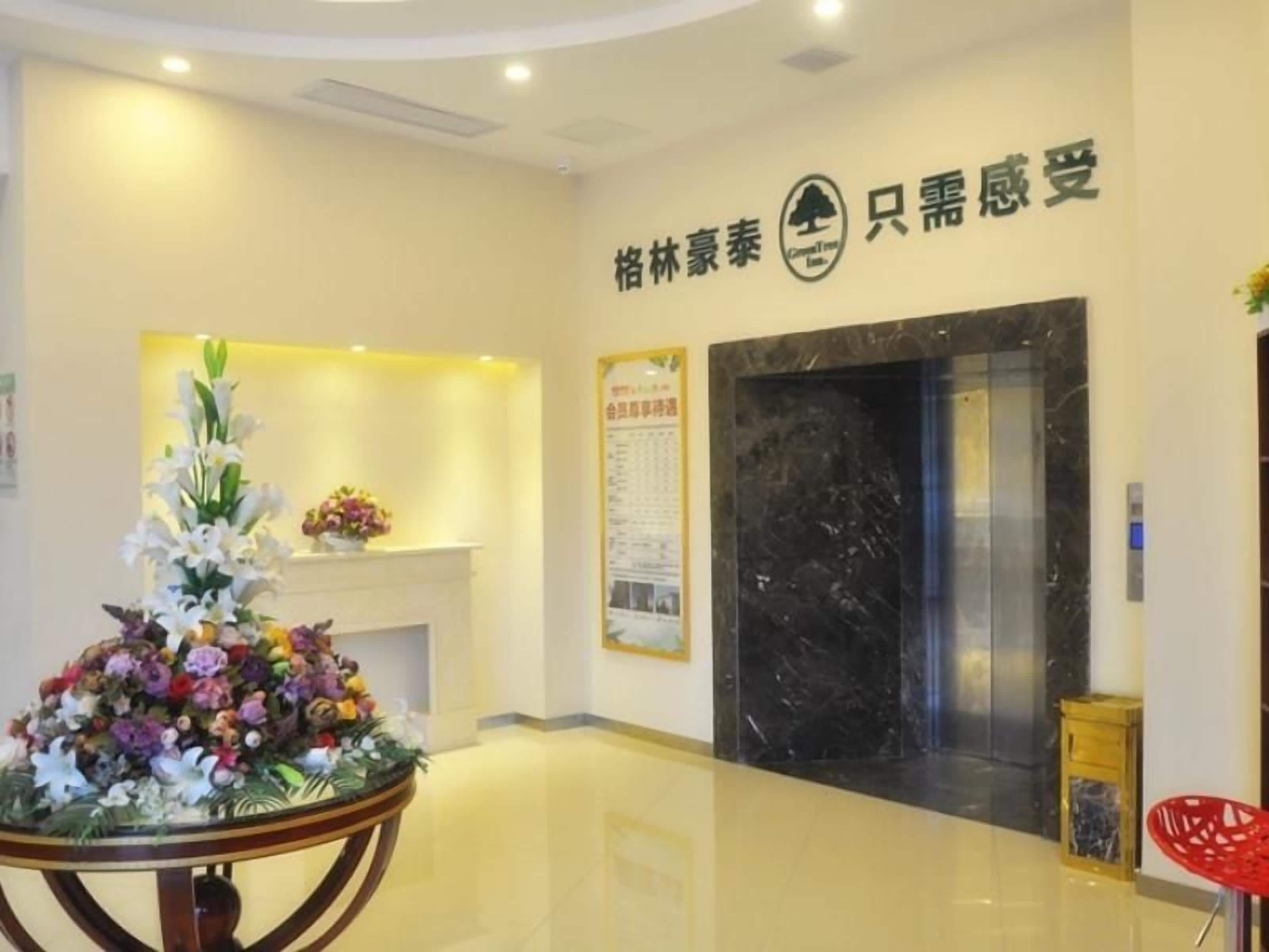 A reception area with a reception desk, a flower arrangement, an elevator, and a wall with signage.