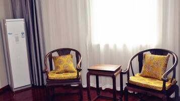 Two wooden chairs with yellow cushions, a small wooden table, and a white refrigerator in a room with wooden flooring and a window with sheer curtains.