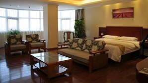 Una habitación de hotel con cama, sofá, silla, una mesita y un ventanal grande.