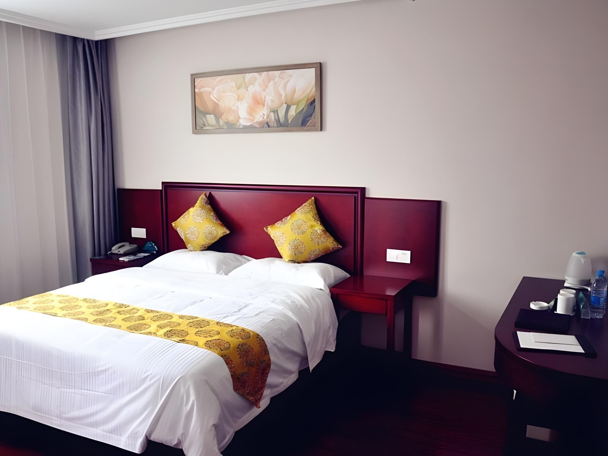 Hotelkamer met een groot bed, twee kussens, een nachtkastje met een telefoon, een schilderij aan de muur en een bureau met een fles water.