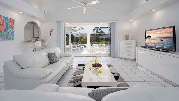 Un salon moderne avec un canapé blanc, une table basse avec des boissons, un téléviseur et une vue sur l’extérieur.