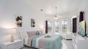 Une chambre à coucher comprenant un lit, une table de chevet, une lampe, une œuvre d’art et une vue sur l’extérieur par une fenêtre.