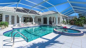 Une grande piscine intérieure dotée d’un toit en verre, entourée de chaises longues et d’un patio couvert.