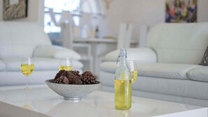 Un salon moderne avec un canapé blanc, une table en verre, un bol de pommes de pin et deux verres de vin blanc.