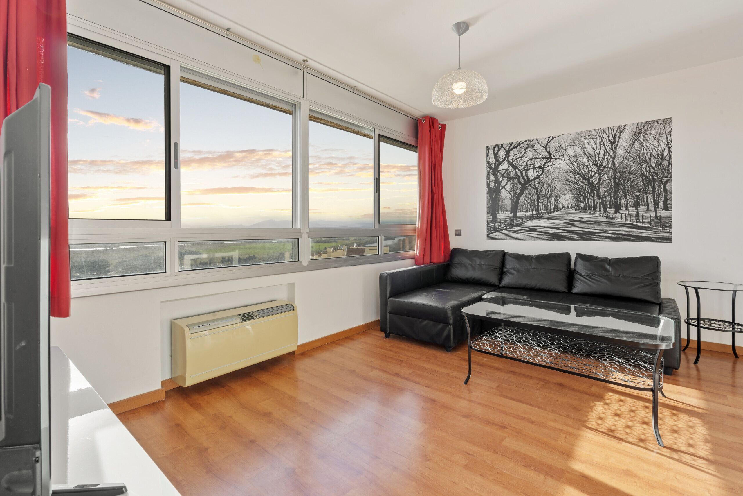 Una sala de estar moderna con un sofá de cuero negro, una mesa de centro de vidrio y vistas a un parque a través de grandes ventanales.