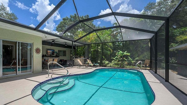 A swimming pool with a glass enclosure, surrounded by lounge chairs and a patio area. - The Edison - Walking Distance to Gulf Course and Edison-Ford Winter Home (Fort Myers)