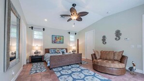 A bedroom with a bed, a ceiling fan, a nightstand, a lamp, a painting, a mirror, and a decorative seahorse on the wall. - The Edison - Walking Distance to Gulf Course and Edison-Ford Winter Home (Fort Myers)