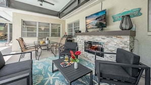 An outdoor patio area with a stone fireplace, seating, and a pool in the background. - The Edison - Walking Distance to Gulf Course and Edison-Ford Winter Home (Fort Myers)