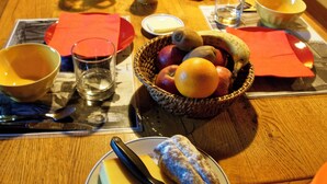 Ein Holztisch ist reichhaltig mit Frühstücksangeboten gedeckt, darunter Käse, Obst und ein Orangensaftkrug.