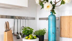 Un piano di lavoro in cucina con un portachiodi, una ciotola di lime, due piante in vaso, un vaso con fiori e un porta utensili a parete.
