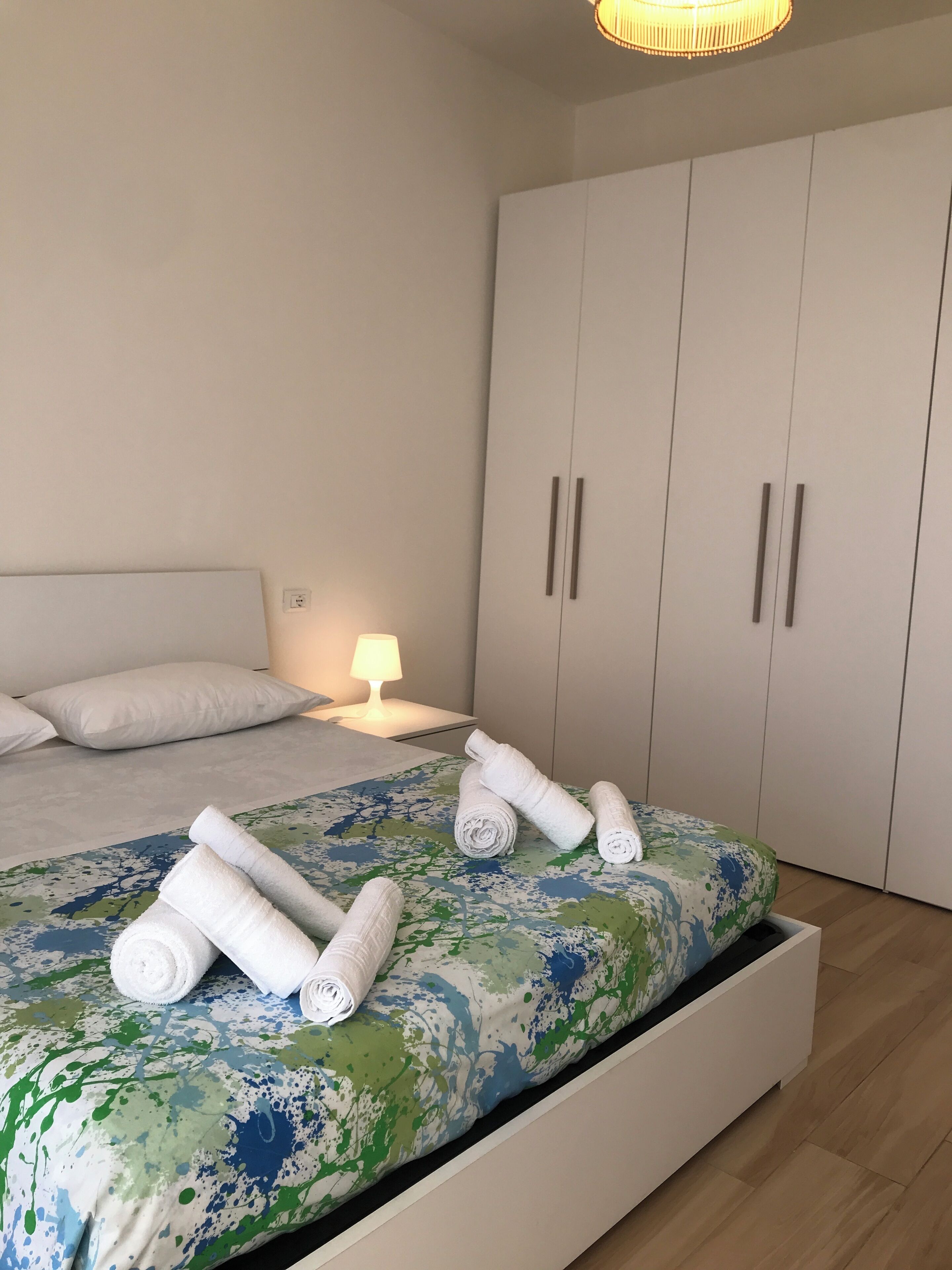 Un dormitorio con cama, almohadas, mesita de noche con lámpara y armario.