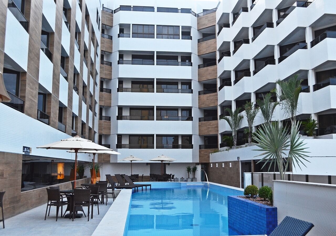 Ein modernes Hotel mit einem zentralen Schwimmbad, Sitzgelegenheiten im Freien und mehreren Balkonen.