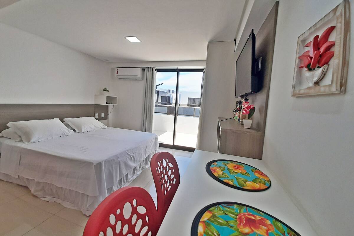 Habitación de hotel con cama, escritorio y silla, televisor y balcón con vistas.