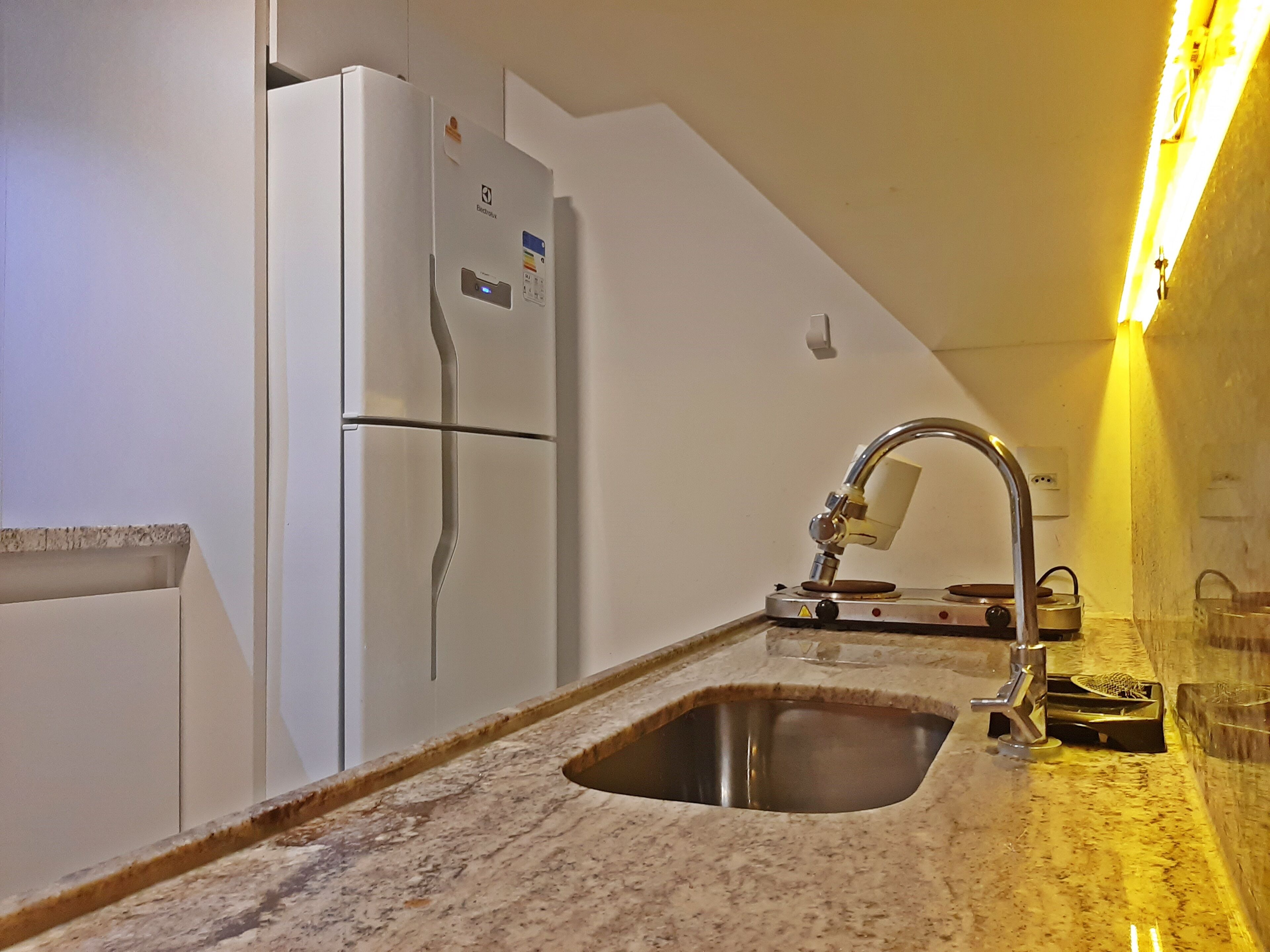 A kitchen with a stainless steel sink, a white refrigerator, and a marble countertop.
