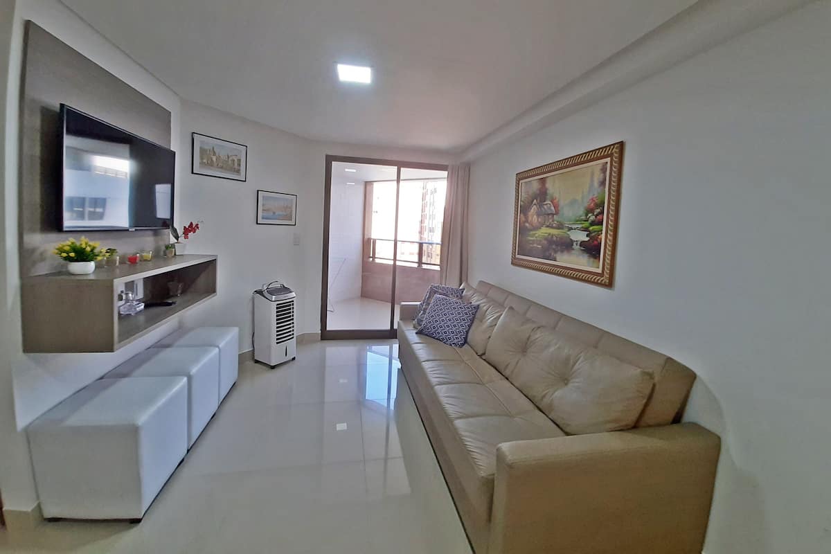 Una sala de estar moderna con un televisor de pantalla plana, un sofá color beige, un mueble de entretenimiento blanco y un cuadro en la pared.