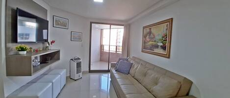 Una sala de estar moderna con un televisor de pantalla plana, un sofá color beige, un mueble de entretenimiento blanco y un cuadro en la pared.
