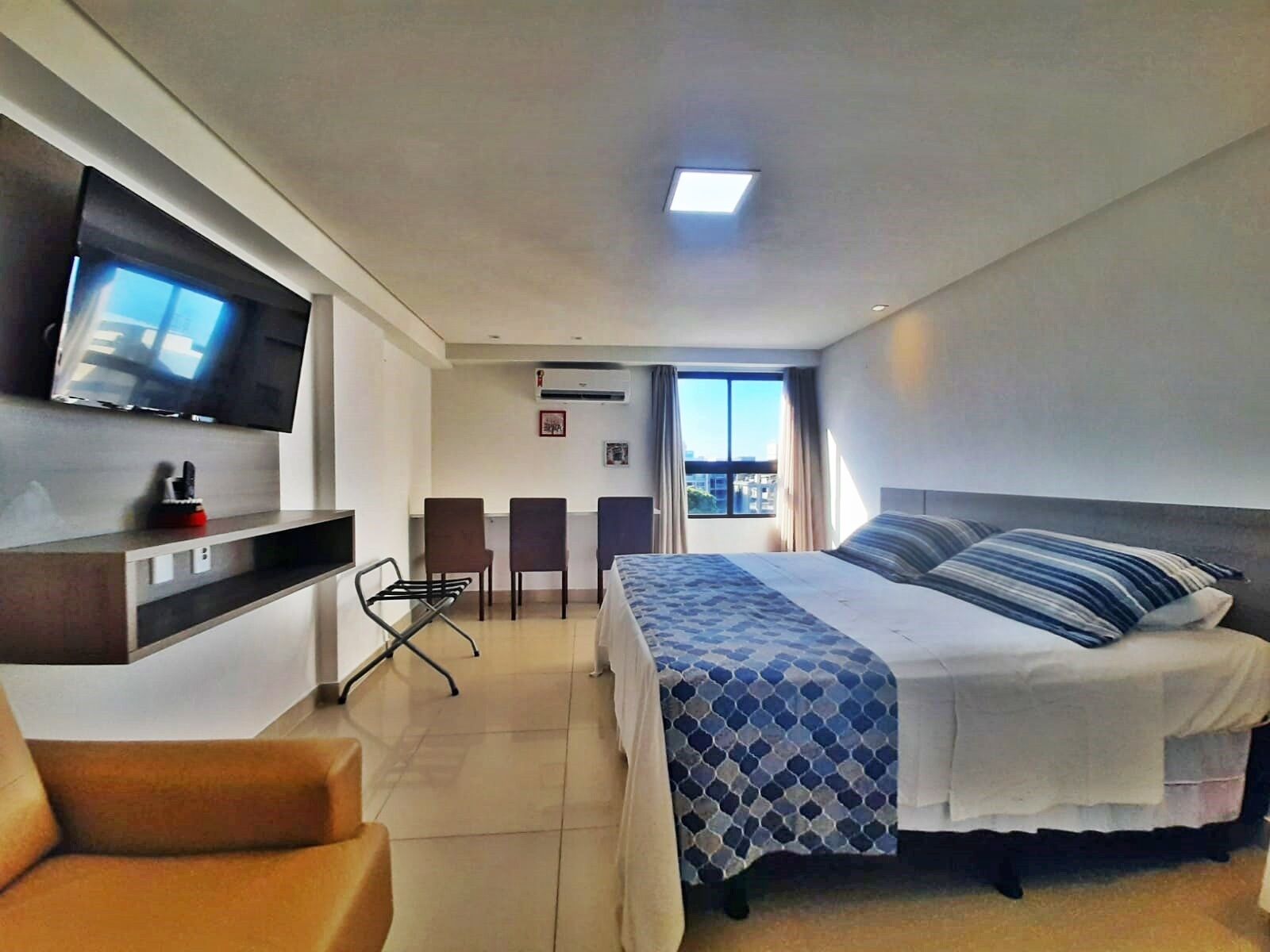 Una habitación de hotel con cama, escritorio con silla, televisor y ventana con cortinas.