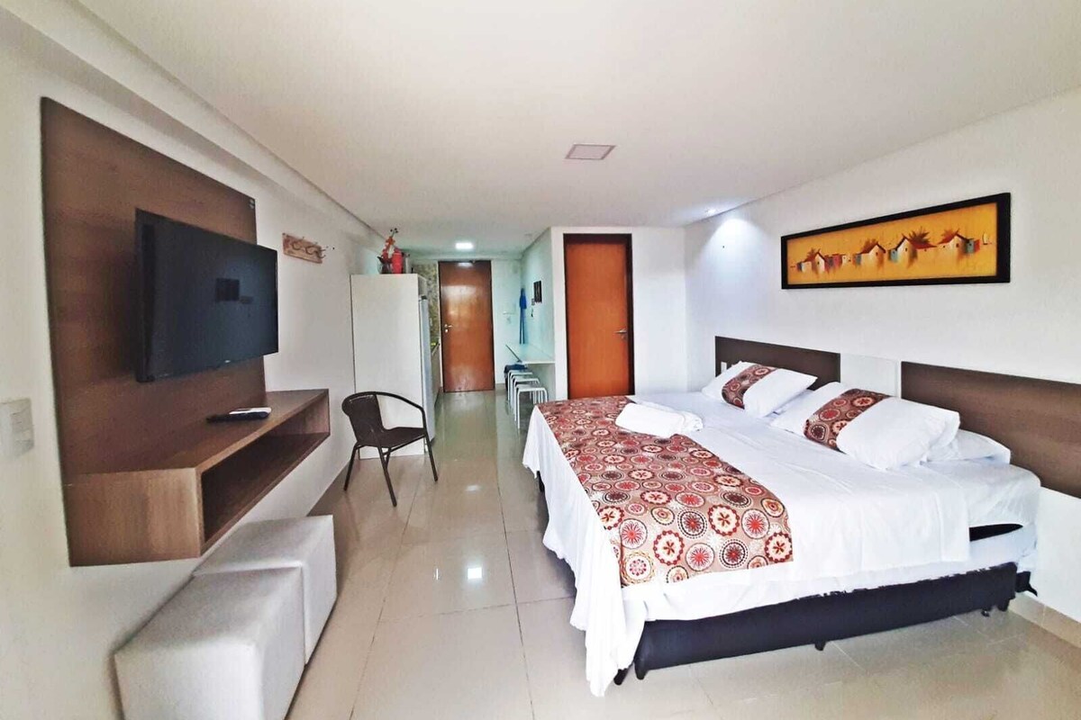 Una habitación de hotel con cama, televisión montada en la pared, escritorio y silla.