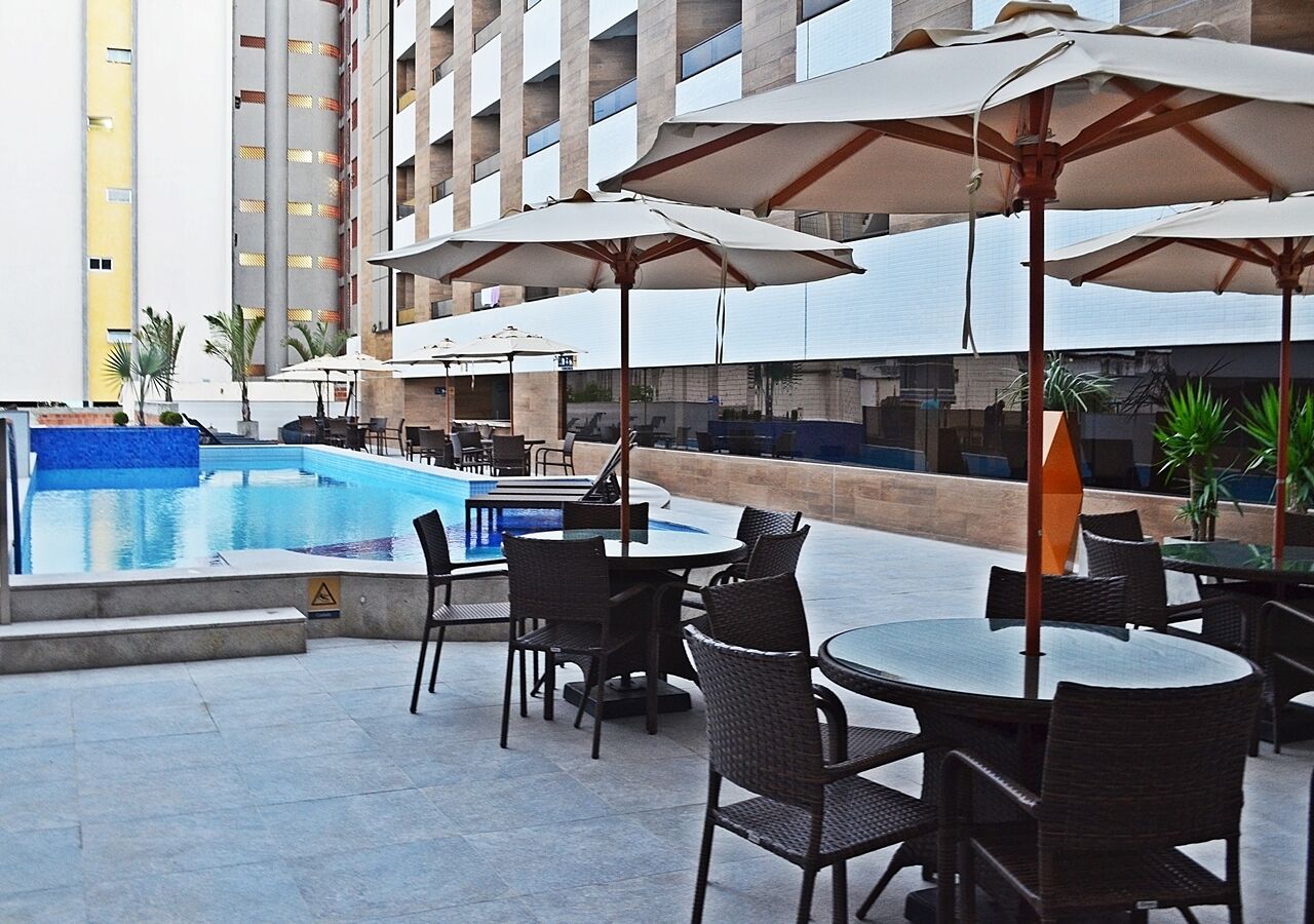 Zona de piscina con mobiliario exterior y sombrillas, rodeada de edificios.