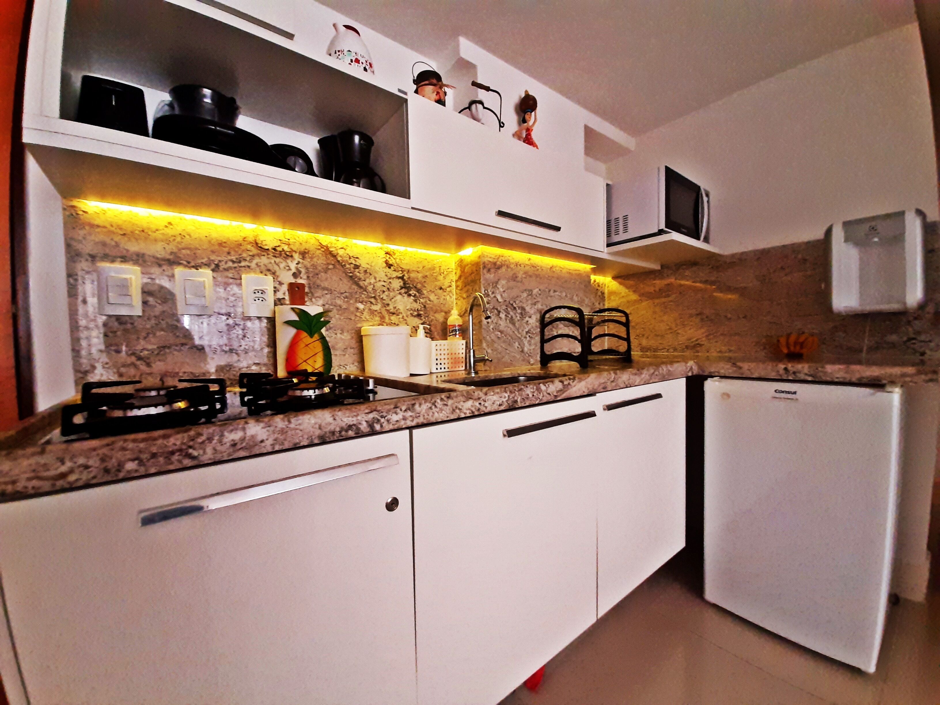 Une cuisine avec des meubles blancs, un plan de travail en granit, une cuisinière à gaz, un four à micro-ondes et un réfrigérateur.