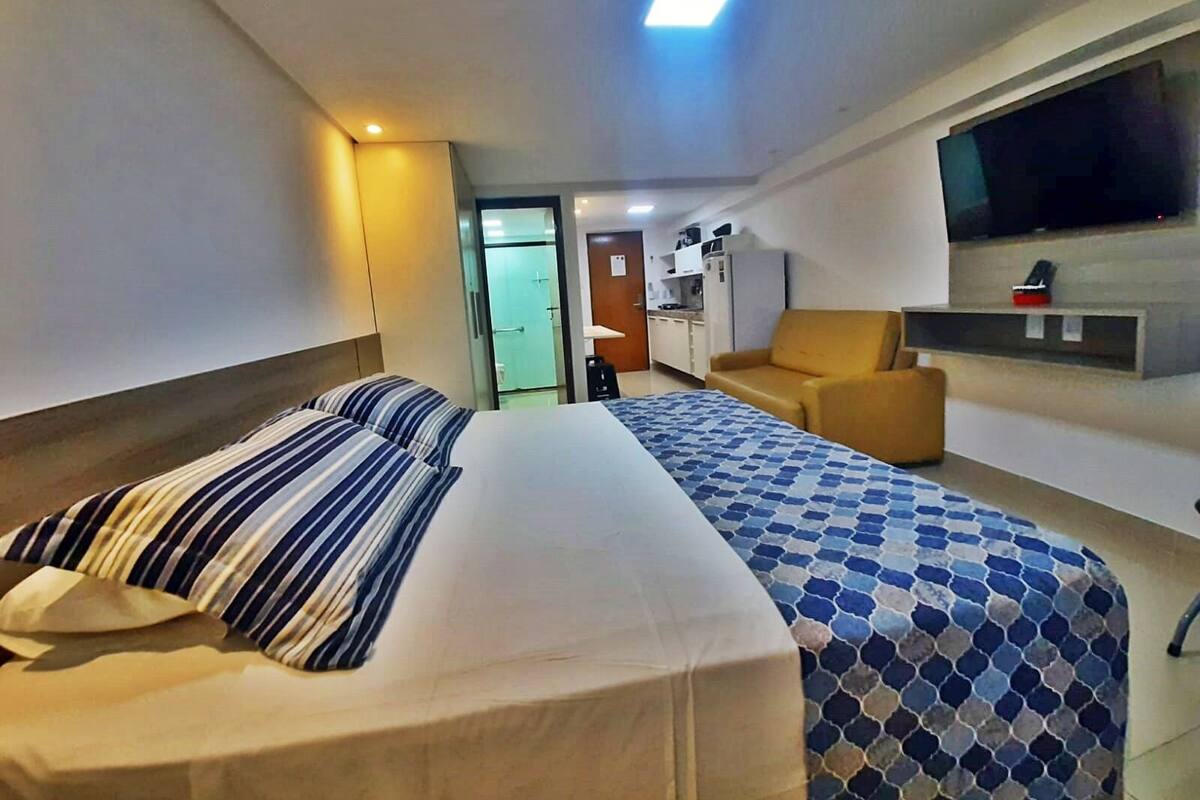 Una habitación de hotel con cama, sofá, televisor y una pequeña kitchenette.
