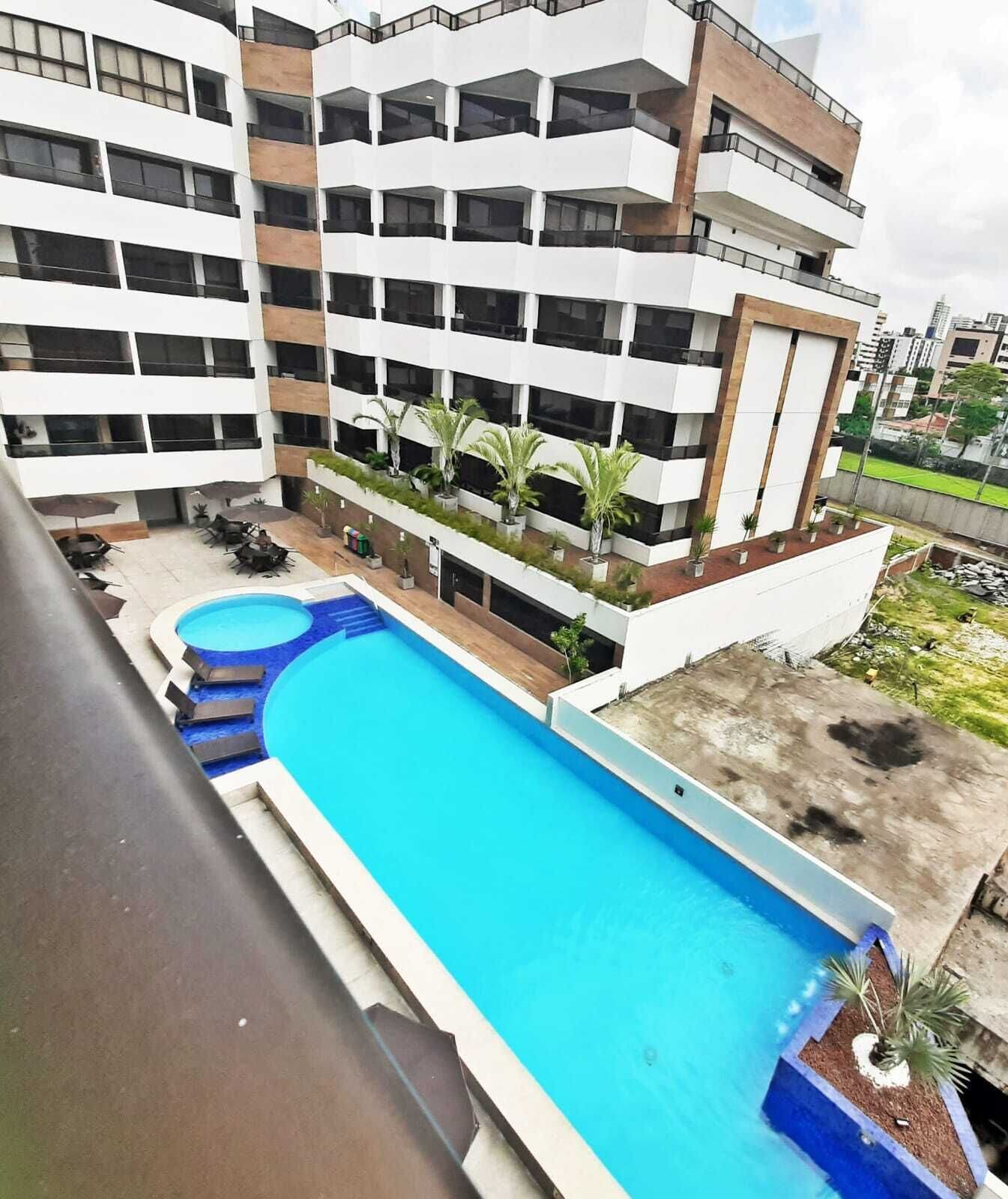 A modern building with a rooftop pool, multiple balconies, and potted plants.