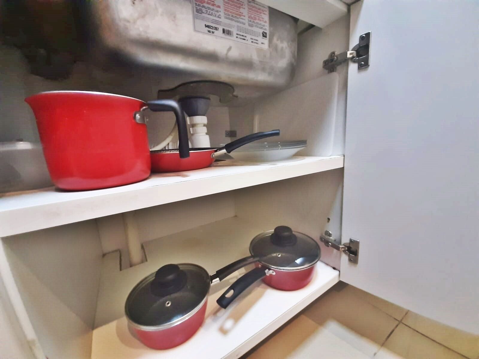 A kitchen with a white countertop, a red pot on the upper shelf, and two red pots with lids on the lower shelf.