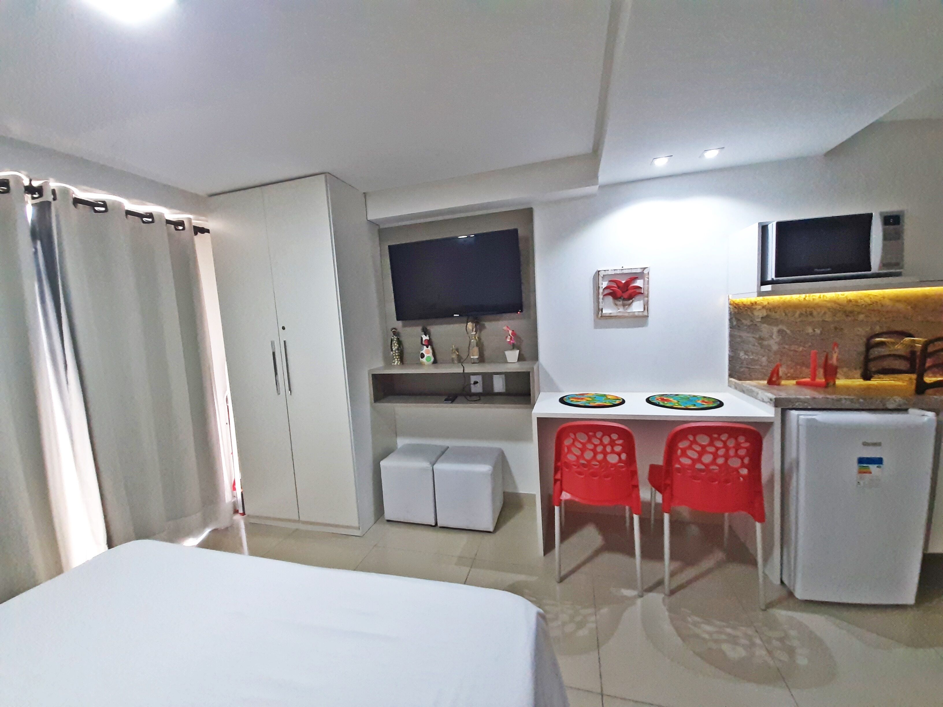 Une chambre d’hôtel compacte comprenant un lit, un bureau avec deux chaises, un petit réfrigérateur et un téléviseur fixé au mur.