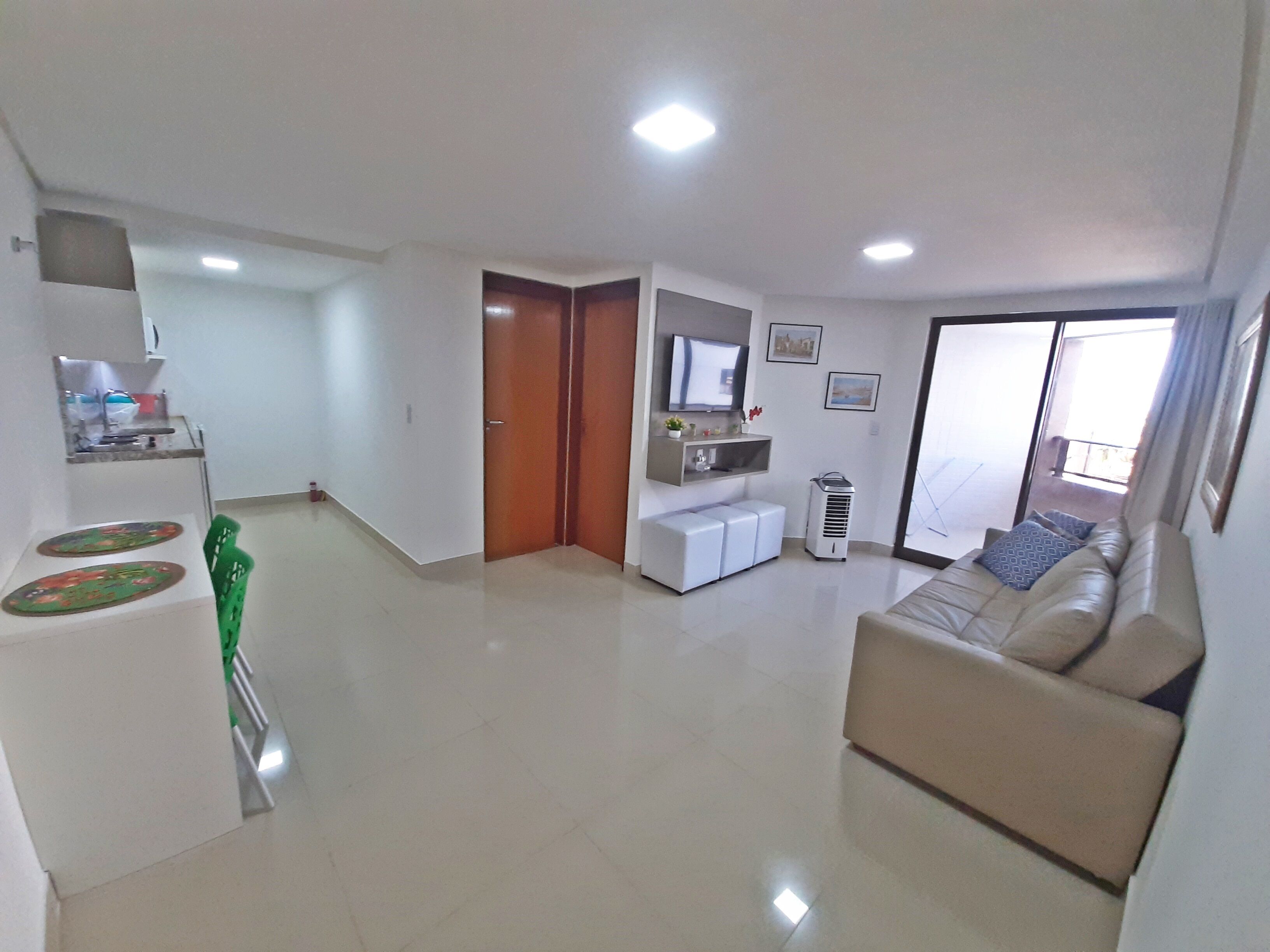 A spacious living area with a sofa, a television, and a sliding glass door leading to a balcony.