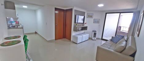 A spacious living area with a sofa, a television, and a sliding glass door leading to a balcony.